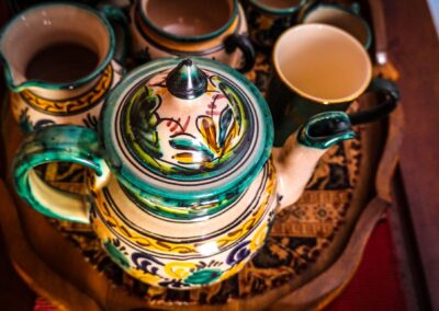 Vibrant handcrafted teapot and cups on an ornate wooden tray, showcasing detailed ceramic artistry.