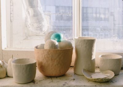 Artistic display of handmade clay pottery and decor on a sunlit windowsill.