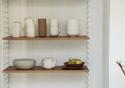 A minimalist ceramic display on wooden shelves featuring pottery and fruits, ideal for interior design inspiration.